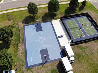 Outdoor residential sports area with a blue basketball court and a separate tennis court, surrounded by grass and trees in Maple Grove.