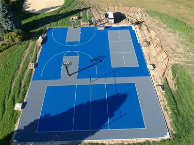 Outdoor residential sports complex with blue and gray surfaces, featuring basketball courts and tennis courts, surrounded by grass and trees in Medina.