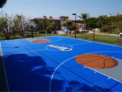  Outdoor residential basketball court with a blue surface, large orange basketball designs, and a white logo.