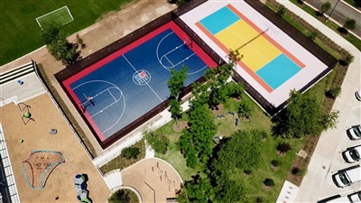 Outdoor sports complex with two courts: one blue and red basketball court with white lines, and one yellow and teal court.