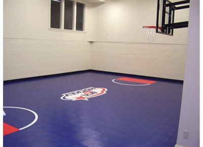 Indoor basketball court with blue flooring, red painted areas, a central logo, and a basketball hoop.