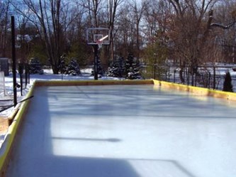 Outdoor ice honkey rink with a small retaining wall and basketball hoop.