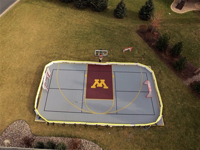 Outdoor multi-sport court with grey flooring and maroon key area with a U of M logo and hockey goals. 