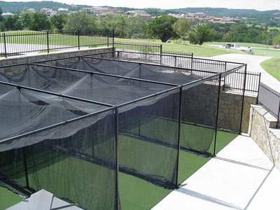 Multiple outdoor batting cages with faux turf and black netting.
