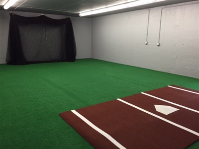 Indoor batting arena with faux turf and batting box with a black net at the end of the room.