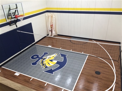 Indoor basketball court with a wood-patterned floor, a gray and blue key area with a large anchor logo, and blue wall padding that features a basketball hoop and a white net in Benton.