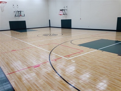 An indoor basketball court with a polished wood surface, green key areas, and a central logo, featuring white and black lines in Burnsville.