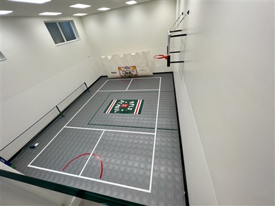 Indoor home basketball court with gray flooring, a green and white logo in the center.