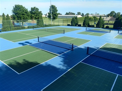 Outdoor sports complex with multiple blue and green tennis courts, tennis nets, and surrounded by trees and greenery.