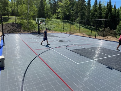 Outdoor residential sports court with a gray surface and red lines, surrounded by trees and greenery in Ramsey.